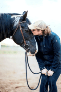 A woman in black jacket and hat kissing a horse.